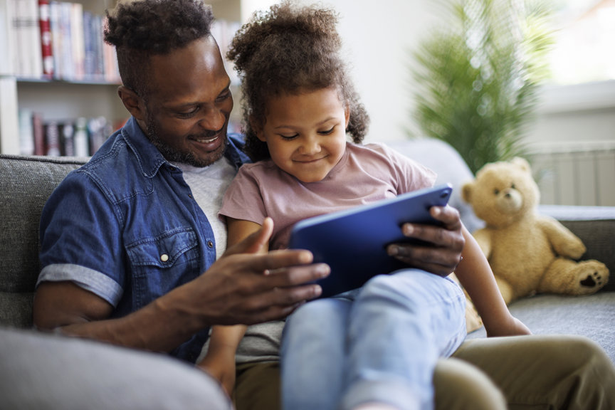 father daughter sitting on a couch using an ipad